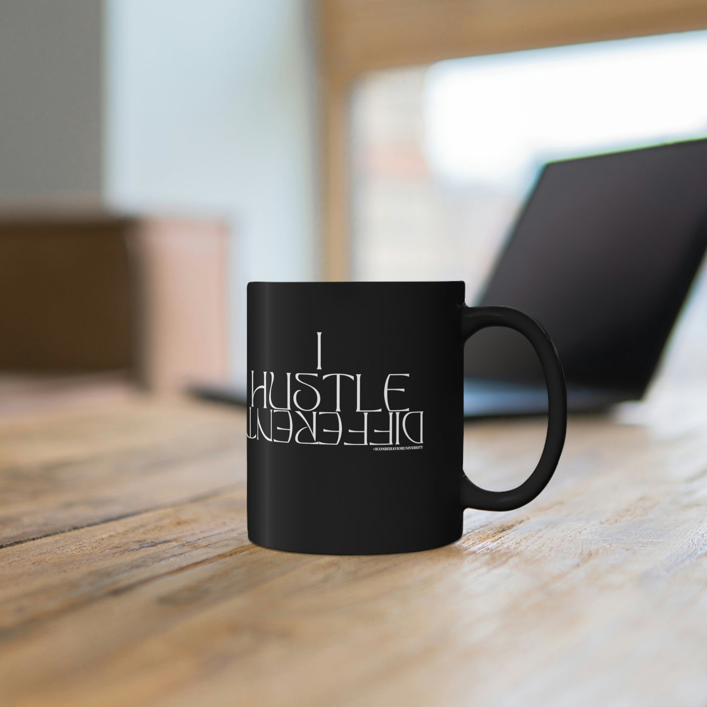 I Hustle Different Black Mug sitting on desk in front of a silver laptop 